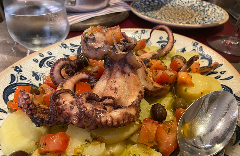 Octopus salad with potatoes, olives, tomatoes, and olive oil on a patterned plate