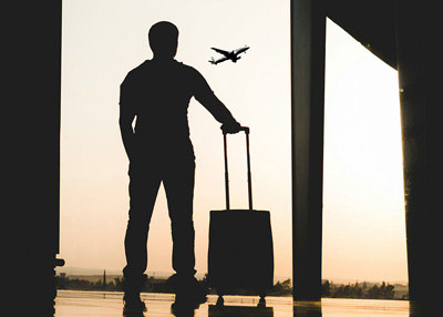 Traveler at airport watching a plane take off with carry-on roller bag.