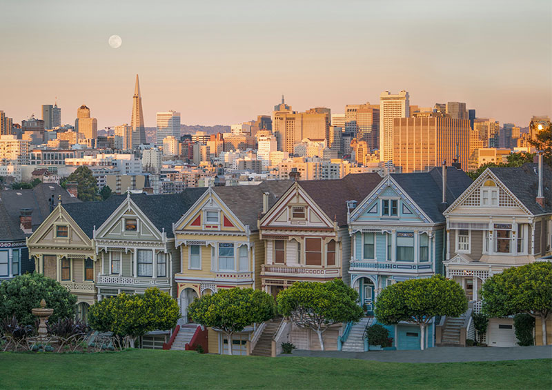 The classic row of colorful Painted Ladies Victorian houses sitting in front of the modern San Francisco downtown skyline at sunset