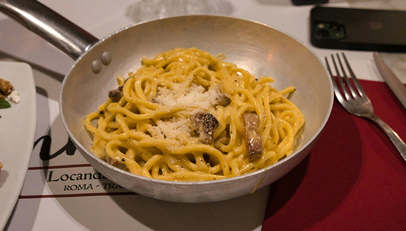 A high-angle, close-up shot of a traditional bowl of Cacio e Pepe pasta served in a rustic Roman trattoria