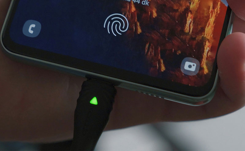 A close-up of a smartphone resting horizontally on a black wireless charging stand with a glowing green indicator light.