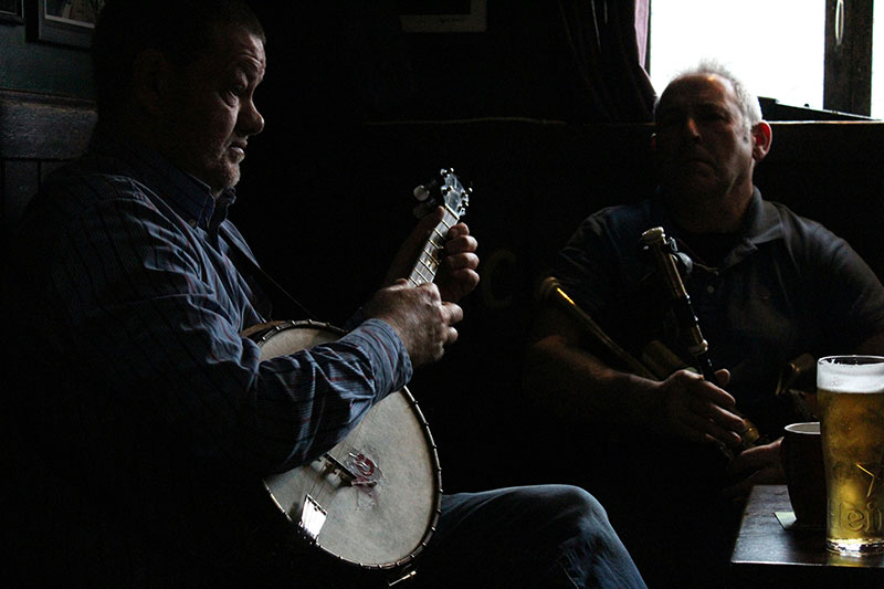 A warm and lively scene inside a traditional Irish pub, showing a group of local musicians gathered in a corner with a fiddle, a tin whistle, and a wooden flute, playing a traditional session for a small crowd of listeners.
