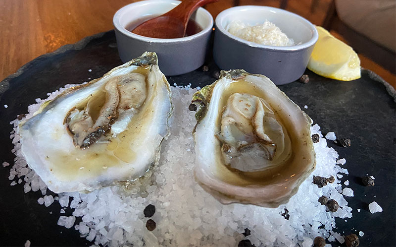 Two fresh oysters on the half shell finished with hot bone marrow flambadou on a bed of rock salt at Porzana.