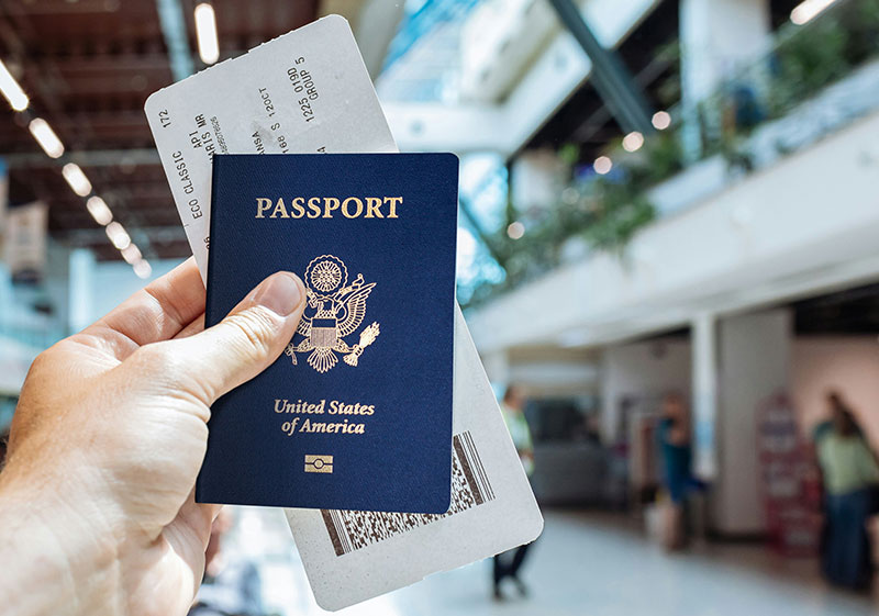 A traveler holding a United States passport and a paper boarding pass in one hand, with a blurred airport terminal background.