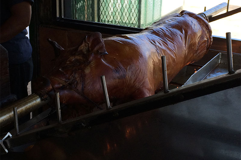 A whole roasted pig head resting on a metal tray, showcasing traditional Puerto Rican lechón preparation.