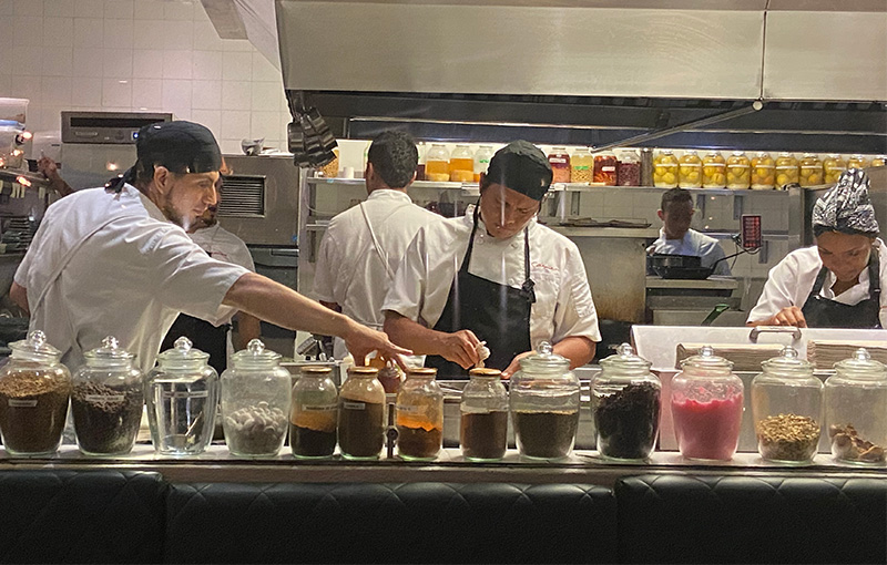 Chefs working meticulously in a bright, open kitchen behind a counter lined with glass jars of spices and ingredients at Restaurante Carmen
