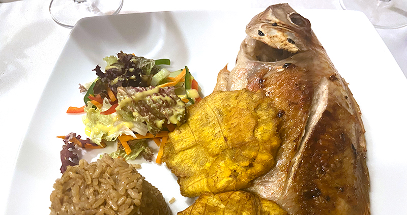 Whole fried fish served with coconut rice and plantains on a white plate