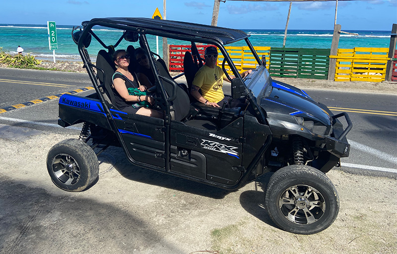 Three people sitting in a black Kawasaki ATV parked on a coastal road next to the bright blue ocean in San Andres.
