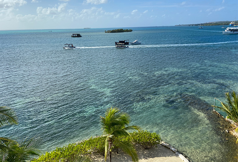 An elevated view of calm turquoise ocean water with small boats and a distant island seen from a condo in San Andres.