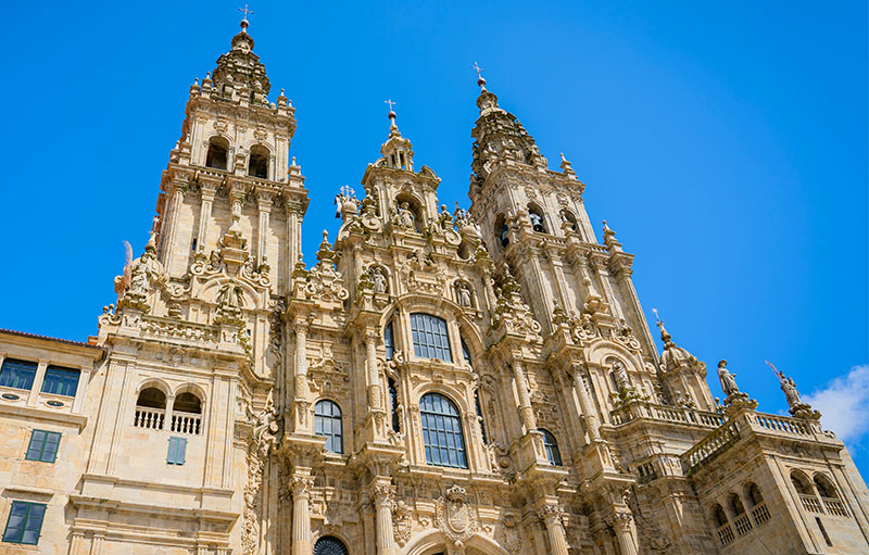 The ornate stone facade of the Cathedral of Santiago de Compostela under a clear blue sky, the final destination of the Camino de Santiago.