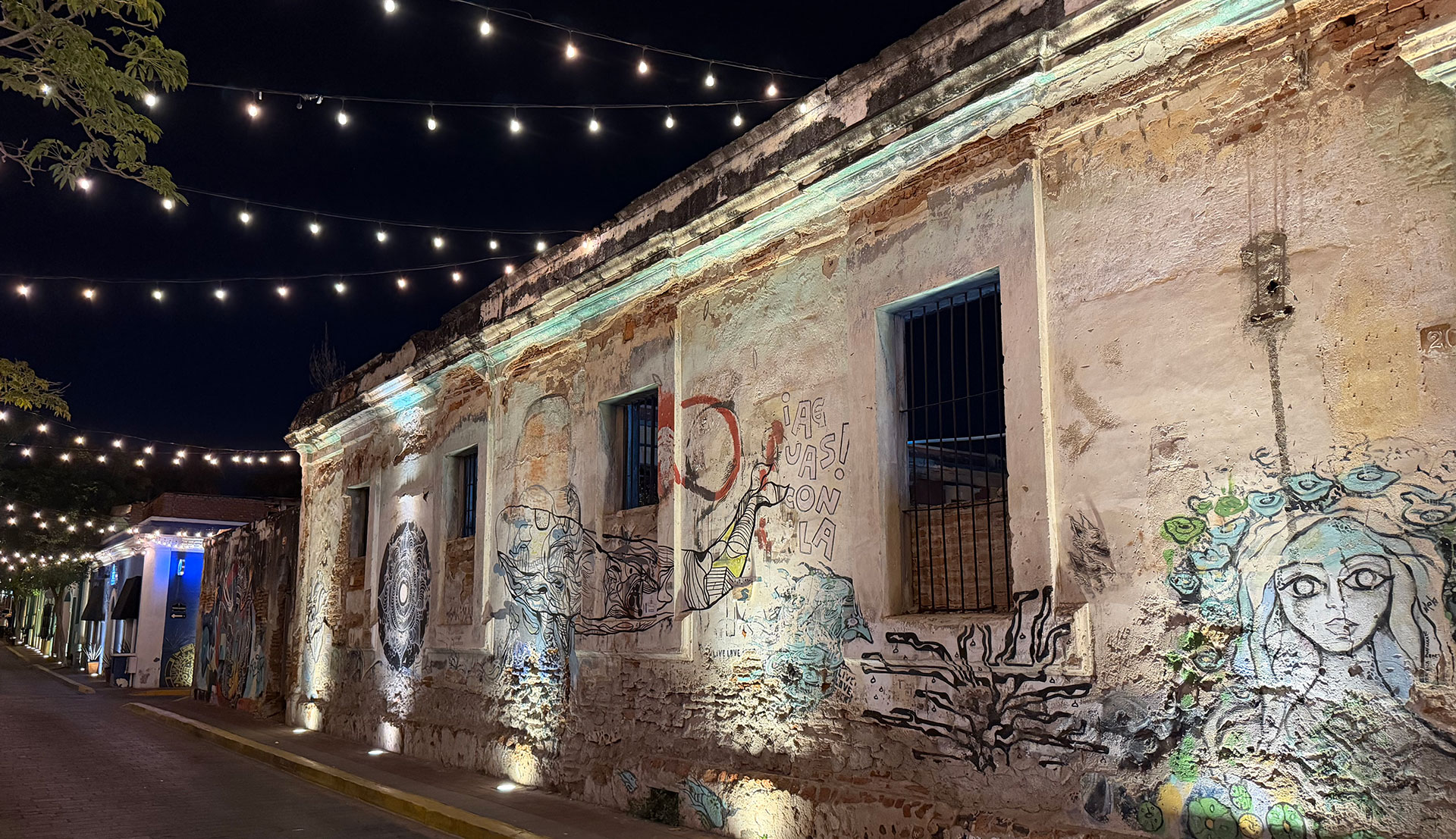 Illuminated cobblestone street at night in Mazatlan's Centro Historico featuring string lights above and historic brick walls covered in vibrant murals.