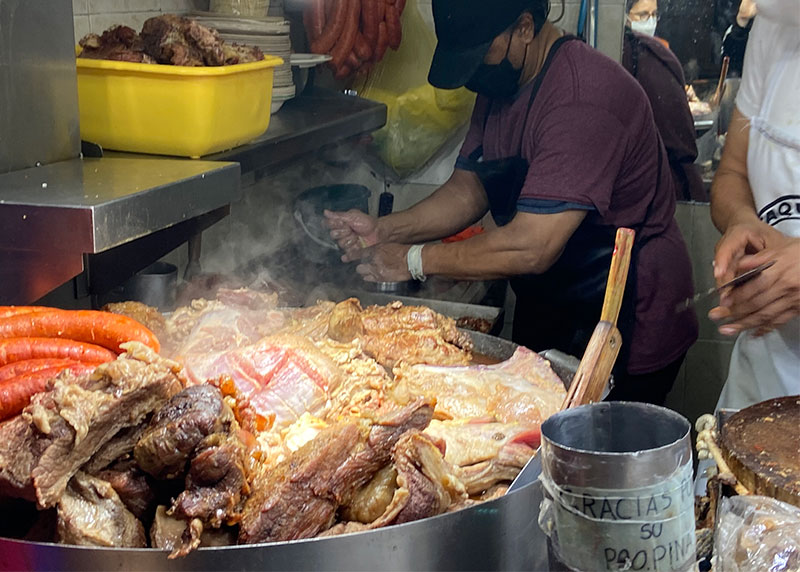 Large hot metal pan filled with suadero meat and longaniza sausage at a busy Mexico City taco stand.