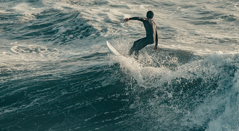 A surfer in a black wetsuit balancing on a white surfboard while riding a wave in the ocean.