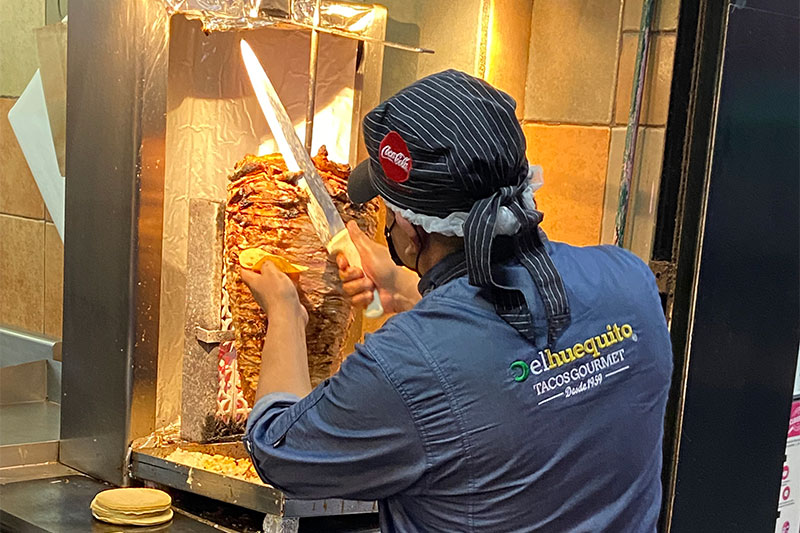 hef slicing al pastor meat from a vertical spit at El Huequito taqueria in Mexico City.