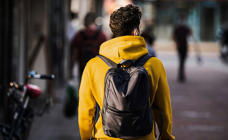 A traveler seen from behind wearing a bright yellow jacket and a dark day pack on the street.