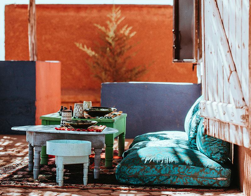 Low-seating outdoor dining area with teal cushions and colorful Moroccan tables.