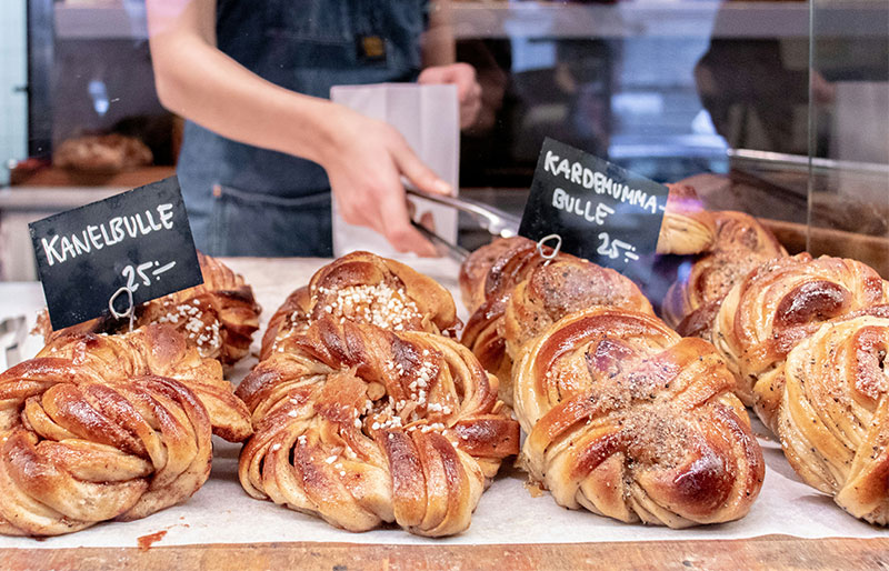Close-up of freshly baked Swedish Kanelbulle (cinnamon buns) and Kardemummabulle (cardamom buns) on a wooden bakery counter in Stockholm.