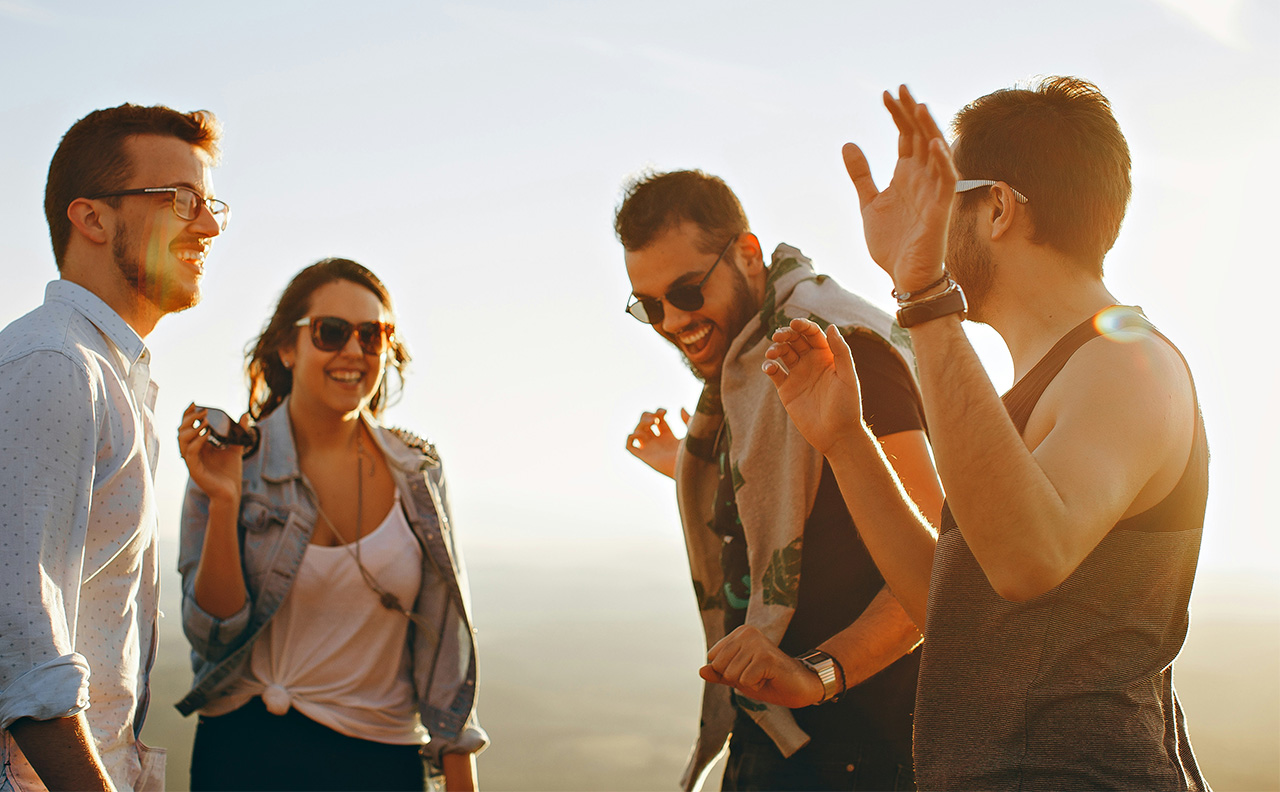 Three young travelers laughing and talking together outdoors against a soft, sun-drenched background, capturing a sense of connection and lighthearted adventure.