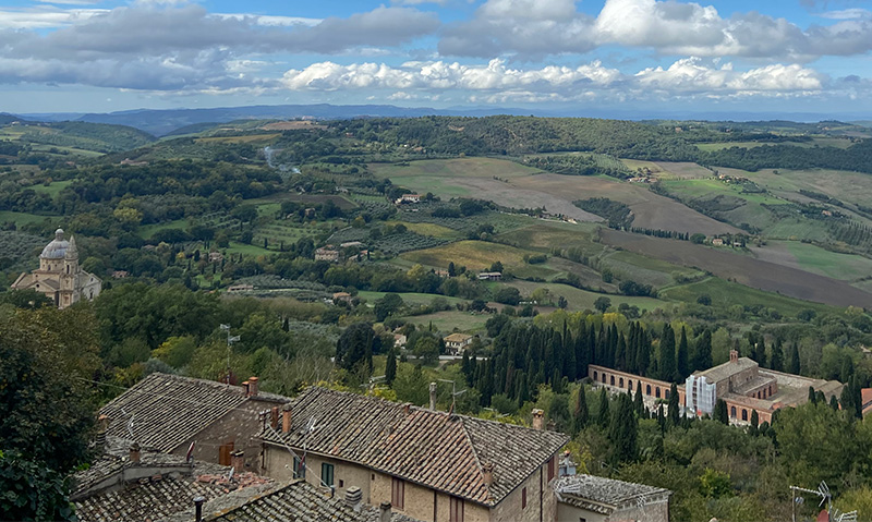 olling countryside in Tuscany with cypress trees, rooftops, and wide views under a dramatic sky