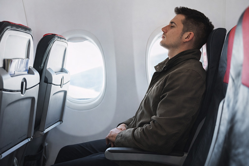 Man sitting on airplane wearing a fall jacket to save luggage space while traveling
