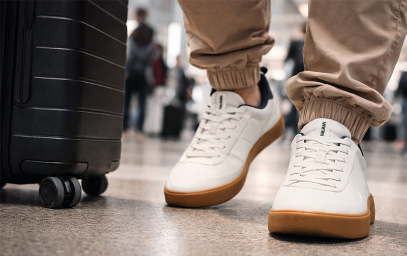 Traveler walking through airport wearing white sneakers with gum soles and pulling a roller suitcase
