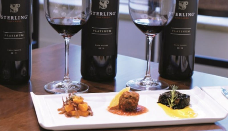 A close-up of a wine pairing experience at Sterling Vineyards, featuring two glasses of red wine on a white rectangular plate alongside small gourmet food pairings