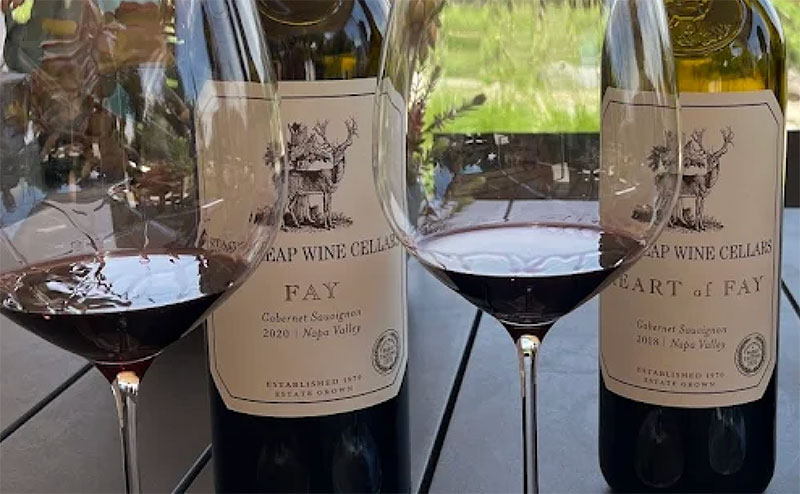 A close-up of a wine tasting at Stag’s Leap Wine Cellars, featuring two glasses of deep red Cabernet Sauvignon on a wooden table next to an open bottle of FAY Vineyard estate wine.