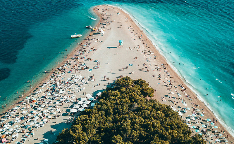 Aerial drone shot of the V-shaped Zlatni Rat pebble beach crowded with sunbathers on Brač island in Croatia.
