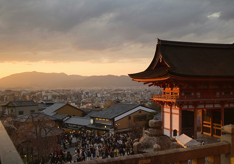 A beautiful view of the Yasaka Pagoda (Hokan-ji Temple) towering over the traditional wooden buildings and sloped stone streets of the Higashiyama District in Kyoto during the soft light of dusk.