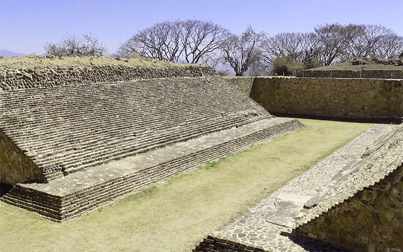 A detailed view of the ancient stone ruins at Monte Albán, showing the weathered textures of the Zapotec archaeological site against a clear blue sky.