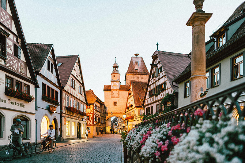 A scenic view of the historic town square in Rothenburg ob der Tauber, Germany, featuring traditional half-timbered houses, cobblestone streets, and vibrant flower boxes under a clear blue sky.