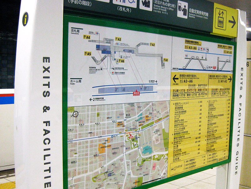 A detailed wall-mounted station map in a Tokyo subway station titled "EXITS & FACILITIES GUIDE," showing a 3D diagram of station levels, exits, and nearby landmarks for both Tokyo Metro and Toei Subway lines.