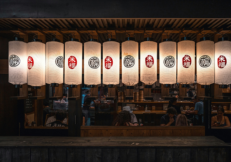 A close-up of a traditional Kyoto-style meal featuring various small bowls of seasonal vegetables, tofu, and pickles, meticulously arranged on a wooden tray in a brightly lit, minimalist restaurant.