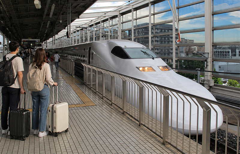 Shinkansen bullet train at Kyoto Station platform with two travelers standing in the foreground holding luggage before boarding.