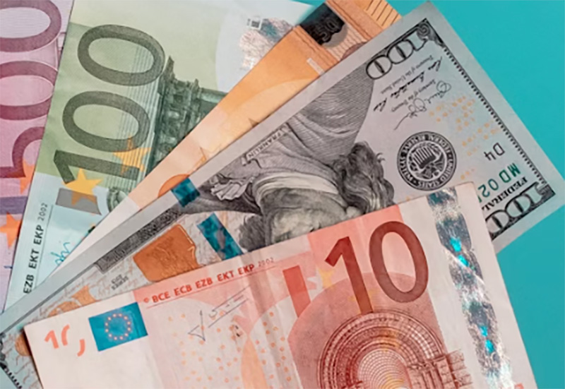 A close-up shot of several different international banknotes being held together, featuring various colors and designs from different global currencies