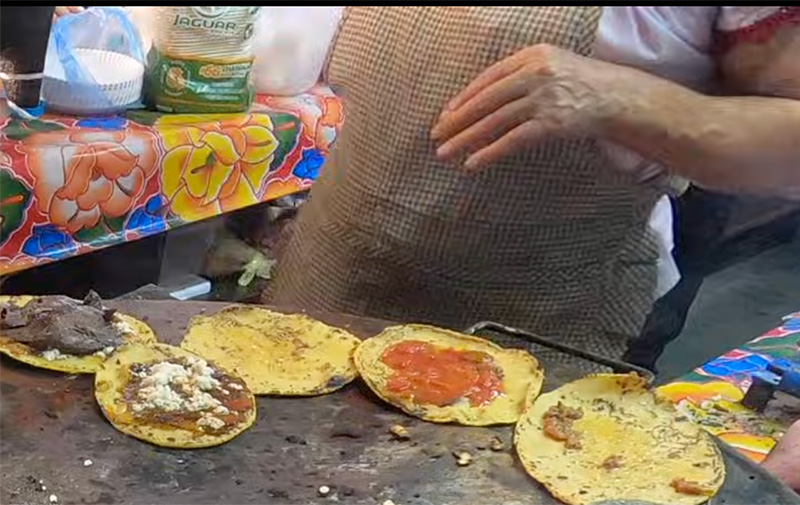 Tacos cooking on a comal in an Oaxaca market food stall