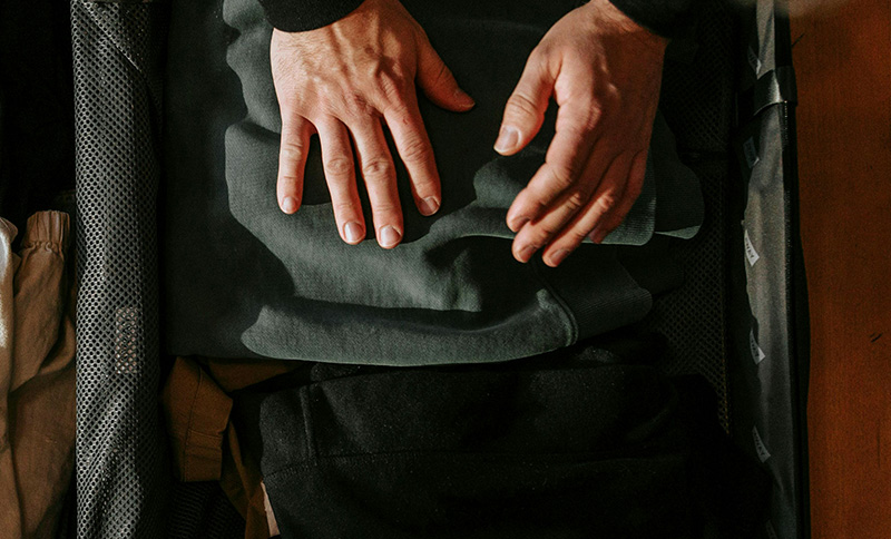 A close-up of a traveler's hands as they carefully pack a dark green garment into a sleek black suitcase, emphasizing a organized and intentional approach to packing light.