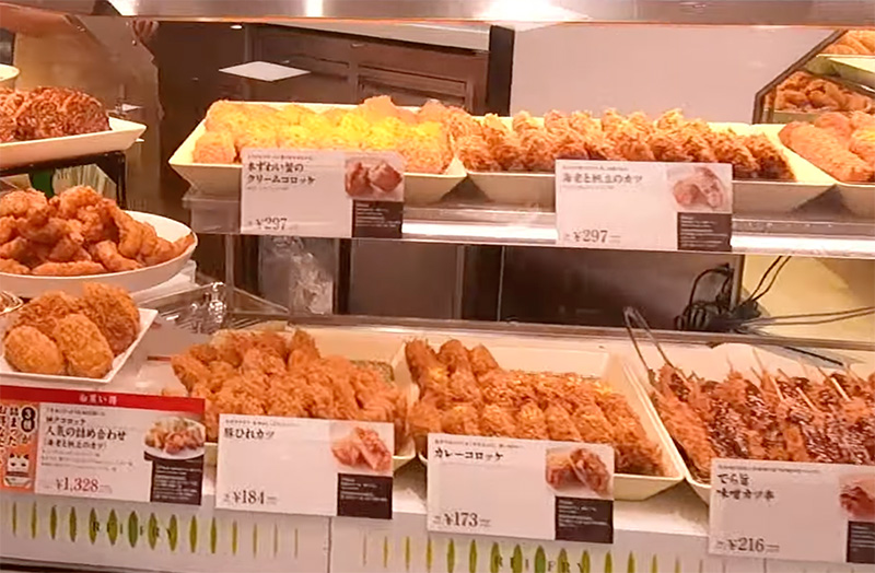 A variety of golden-brown fried foods, including tonkatsu and croquettes, neatly displayed in a glass case at a Tokyo department store basement food hall (depachika).