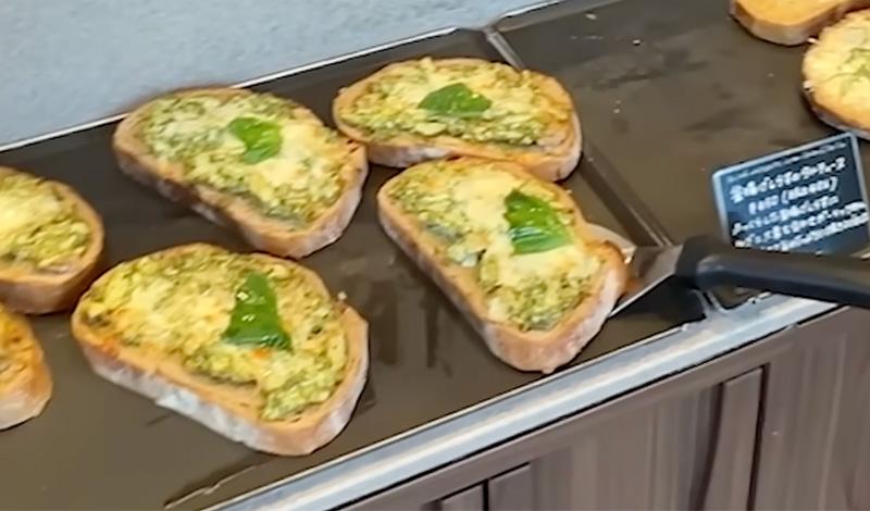 Four slices of thick-cut Japanese milk bread toast topped with melted cheese and fresh green herbs, served as a quick morning meal in a Tokyo bakery.