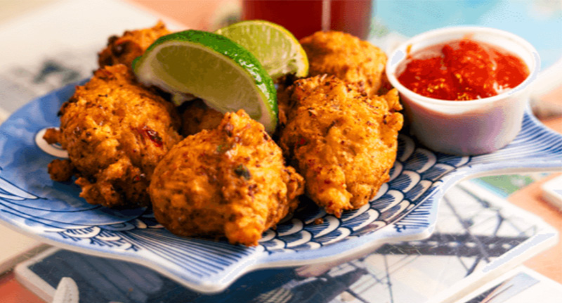 A golden-brown basket of crispy conch fritters served with a side of dipping sauce and fresh lime wedges on a tropical-themed plate