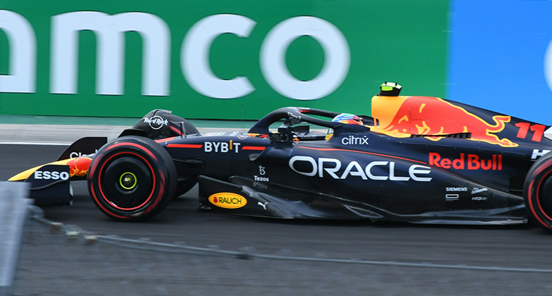 A high-speed view of a Formula 1 car racing down a palm-lined street circuit in Miami, with the modern stadium and grandstands visible under a bright, clear sky.