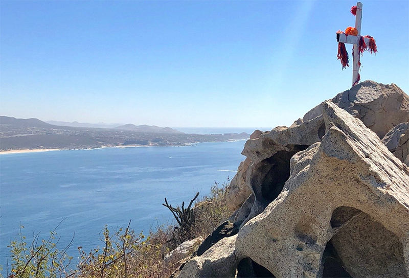 A panoramic view from the summit of Mt. Solmar in Cabo San Lucas, looking down at the narrow strip of land where the golden sands of Lover's Beach and Divorce Beach meet, surrounded by deep blue ocean and rugged cliffs.