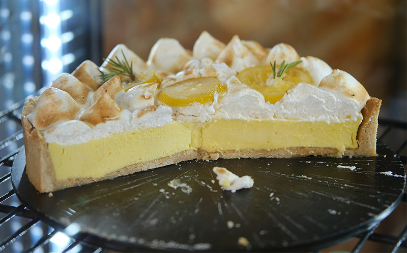 A close-up of a generous slice of Key Lime Pie, featuring a thick graham cracker crust, a smooth pale yellow citrus filling, and a high peak of toasted meringue, served on a white plate.