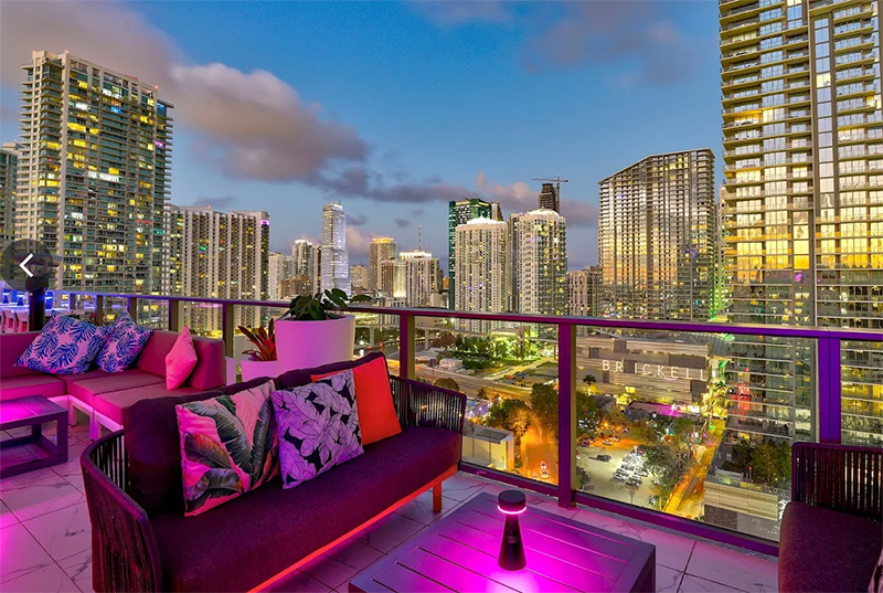 ibrant rooftop scene at Rosa Sky bar in Brickell, featuring glowing pink neon lighting, modern lounge seating, and a panoramic view of the Miami skyline at night.