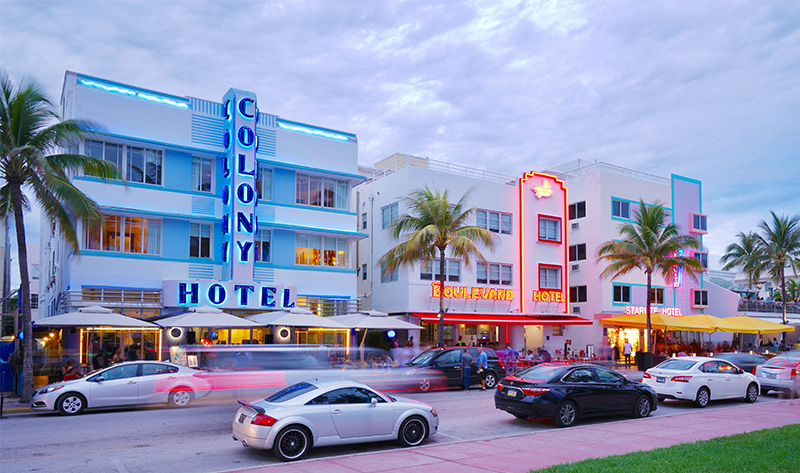 A view of the South Beach shoreline featuring several colorful, Art Deco-style lifeguard stands on the sand, with the turquoise ocean and a clear blue sky in the background.