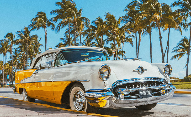 Classic yellow and white vintage car parked along a palm-lined street in South Beach Miami
