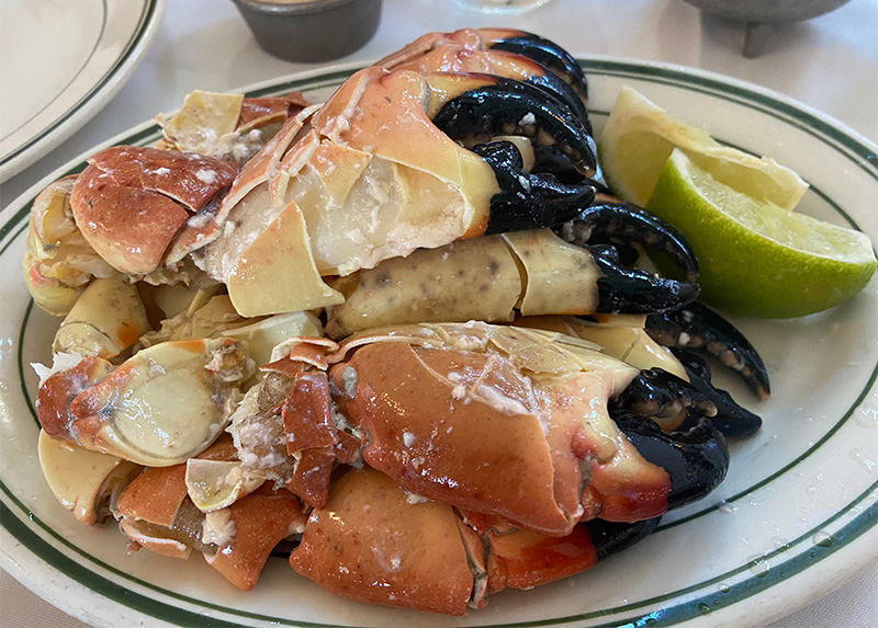 A close-up, top-down shot of a platter featuring several chilled stone crab claws served with a side of mustard dipping sauce and a fresh lime wedge on a white plate.