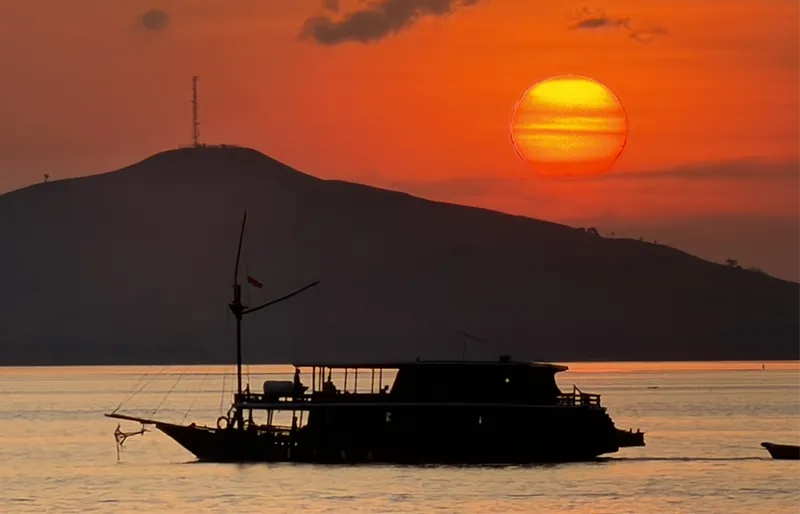 Vibrant orange and pink sunset sky casting a warm glow over calm waters and rugged island silhouettes in Komodo National Park.