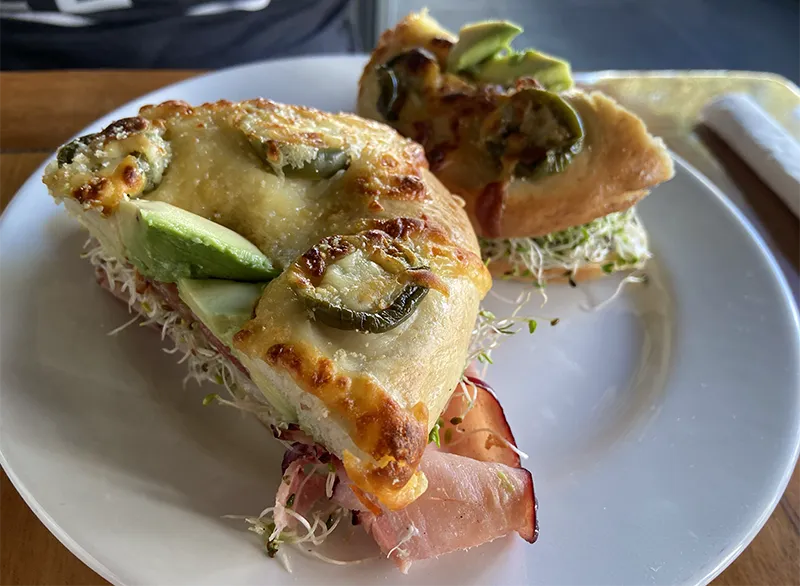 A halved bagel breakfast sandwich filled with egg and greens on a plate at Rico's Café.