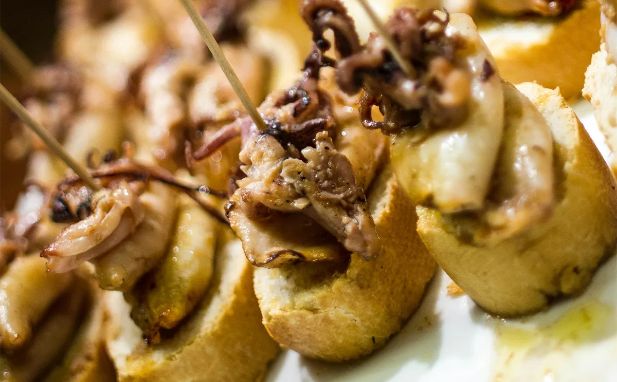 San Sebastián Pintxo Crawl hero image showing a traditional bar counter stacked with vibrant Basque pintxos under warm lighting.